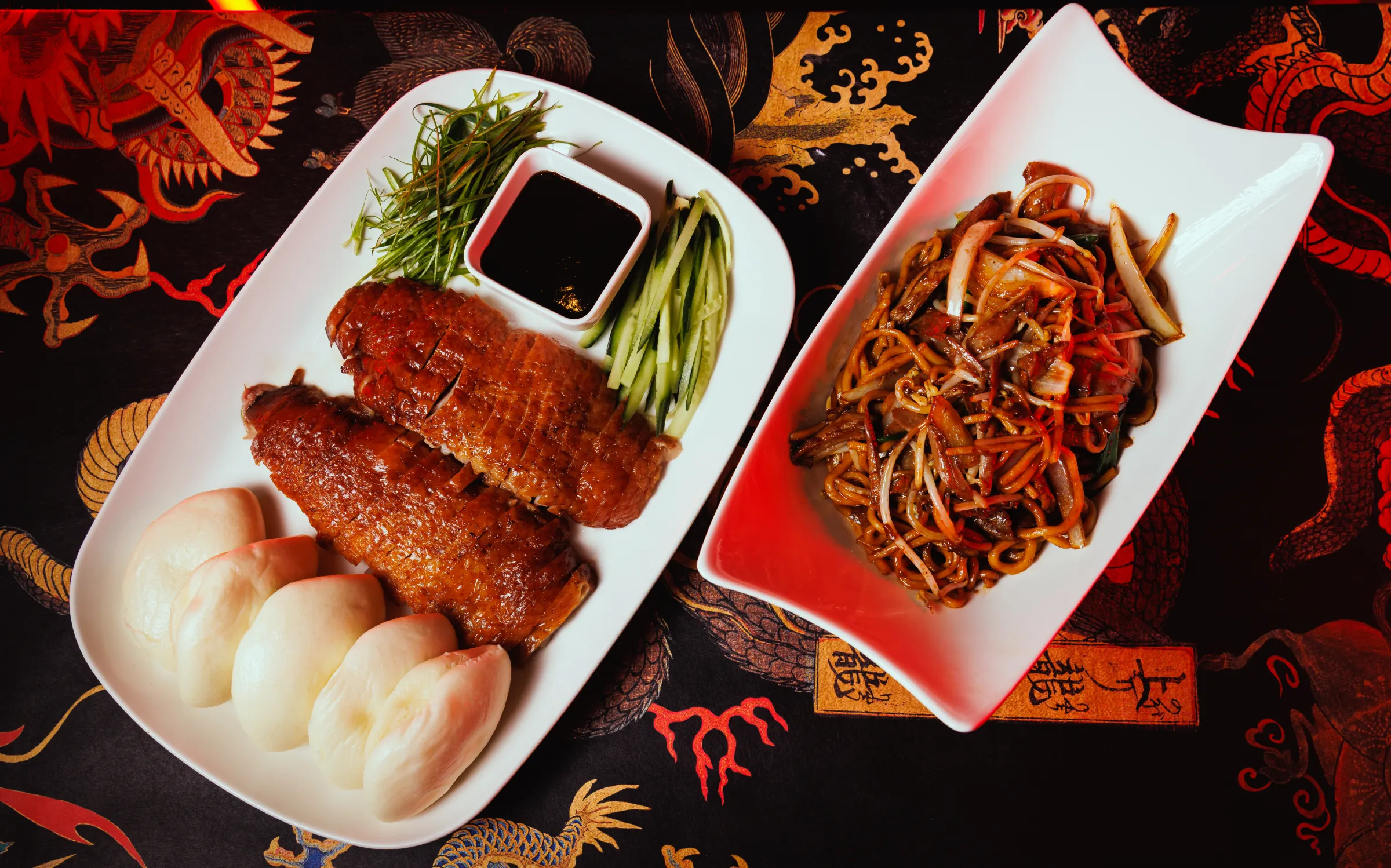 A huge serving of duck lo mein and a crispy duck platter with steamed buns and all the fixings.