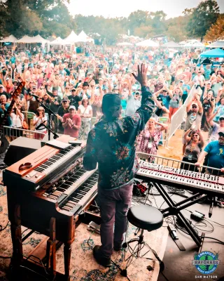 view from stage of performer at keyboards waving at crowd of outdoor audience