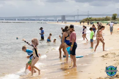 photo of people on shore of a beach with bridge in background enjoying themselves