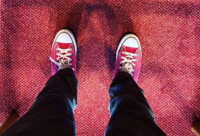 photo from above of legs wearing black pants and red converse sneakers on red carpet