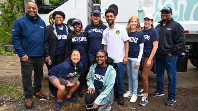 Mayor poses with group of 10 volunteers wearing Hopkins sweatshirts, 2 kneeling in front