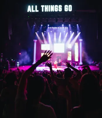 View from far row of stage lit up with performers and 'ALL THINGS GO' above stage in block letters