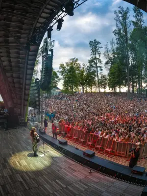 solo performer stands in a spotlight with guitar and mic looking out at crowd during outdoor daytime performance