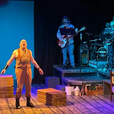 man on stage singing with band on raised platform behind him