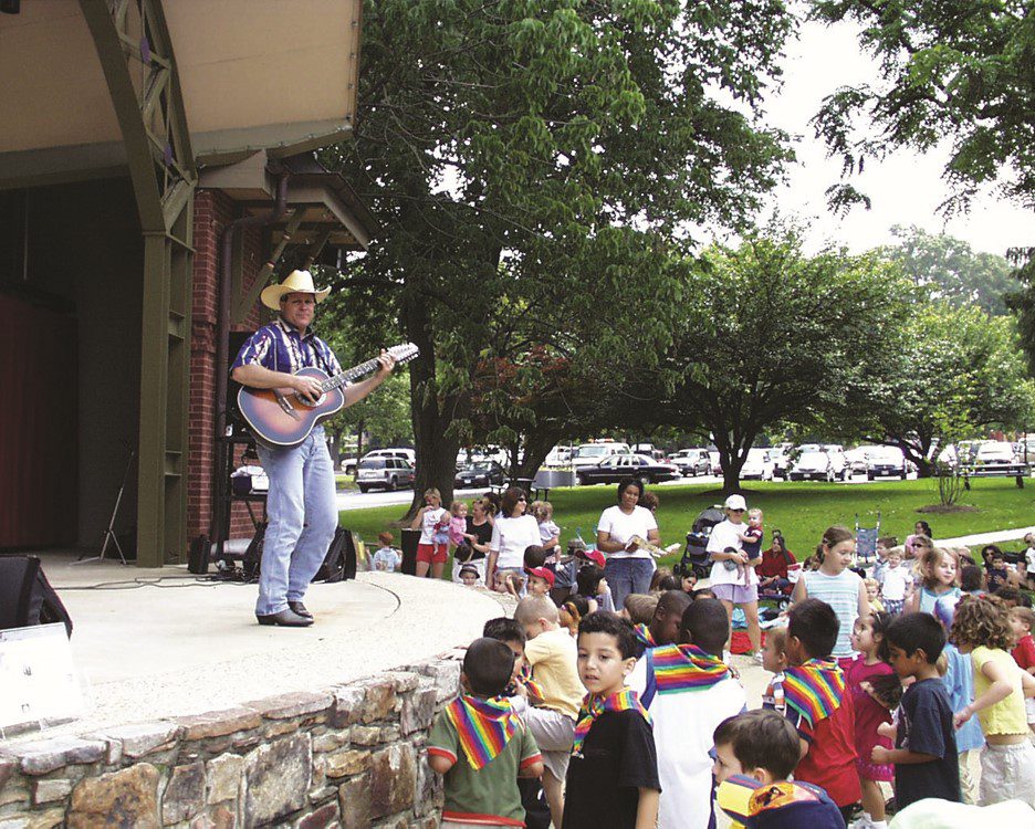 man playing guitar on stage with children listening and dancing