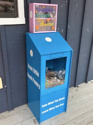 blue Little Free Food Pantry on wooden porch outside dark blue cottage wall