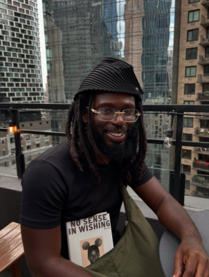 man sitting on a balcony of a city building smiling with book on lap