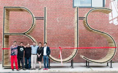 "BUS" sculpture made of wood, 5 people standing in front of it